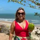 Foto de Amanda Soares sorrindo em uma praia, usando maiô vermelho e segurando um coco