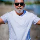 Foto de Fran de Almeida sorrindo em uma praia, usando camiseta branca e óculos escuros